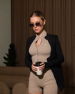 Beige AIRE contour romper with fitted design, sleeveless style, and scoop neckline, displayed on a hanger.