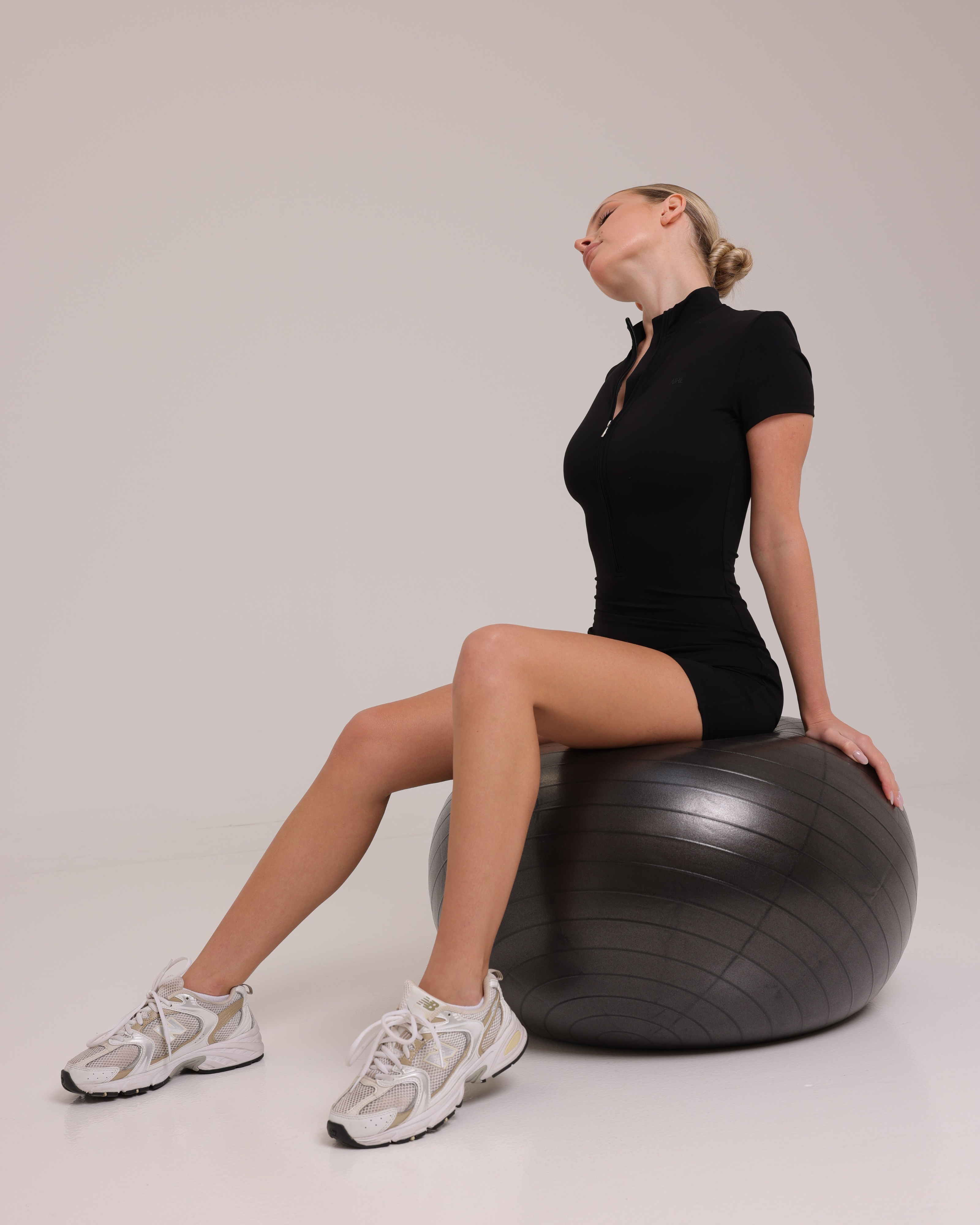 A black AIRE Sculpt Romper displayed on a model, showing its fitted design and sleeveless style for a sleek, modern look.