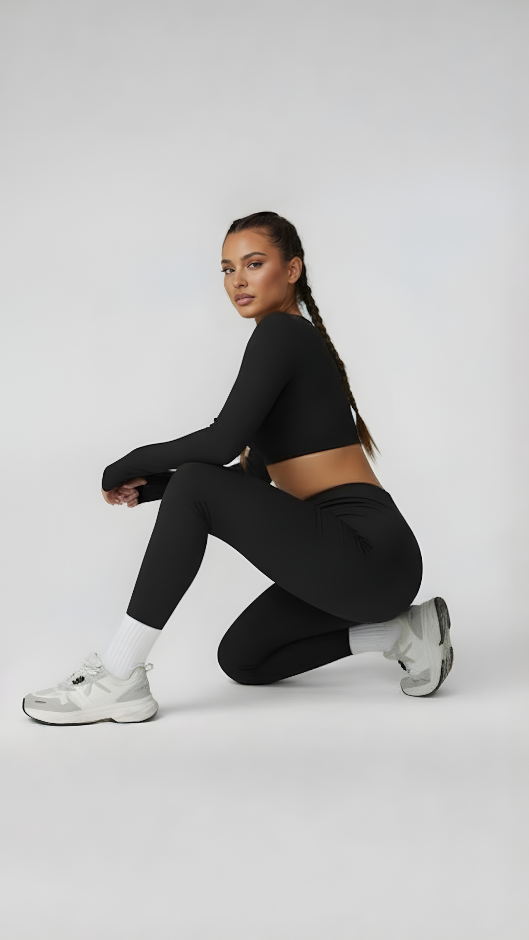 Woman in black long sleeve crop top and leggings kneeling, wearing white sneakers