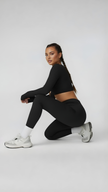 Woman in black long sleeve crop top and leggings kneeling, wearing white sneakers